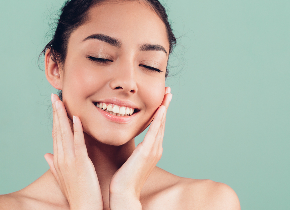 Dental Implants Del Mar: Natural, Confident Smile Results Woman gently cradling her smiling face with her eyes closed, representing the natural-looking results dental implants can help restore