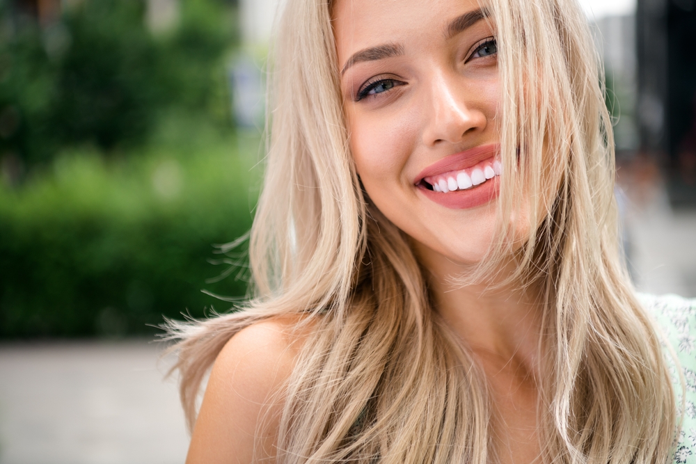 Bright Smile Outdoors: Veneers Results in the La Jolla Area Woman smiling outdoors with a bright, white smile, the kind of result veneers can help patients in the La Jolla area achieve