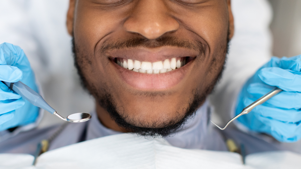 Healthy Smile Checkup: Bearded Patient with Dental Instruments Smiling bearded man with gloved hands holding a dental mirror and explorer near his face in the San Diego area