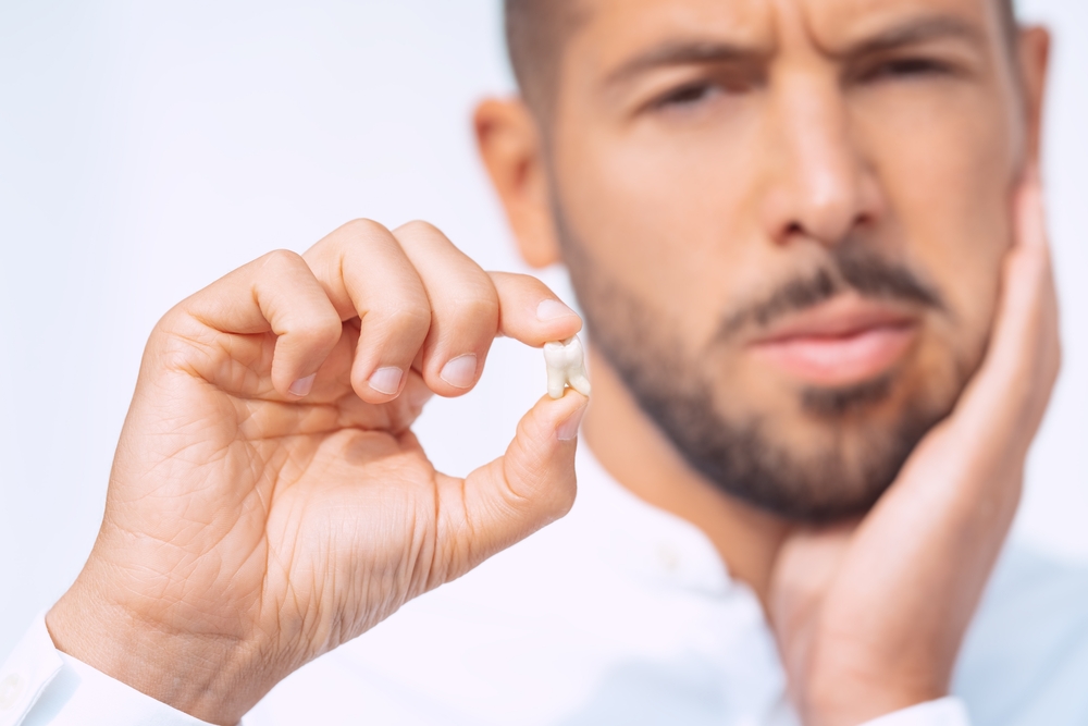 Tooth Pain Relief: Man Holding Extracted Tooth Before Treatment Man wincing in tooth pain while holding an extracted tooth in the La Jolla area