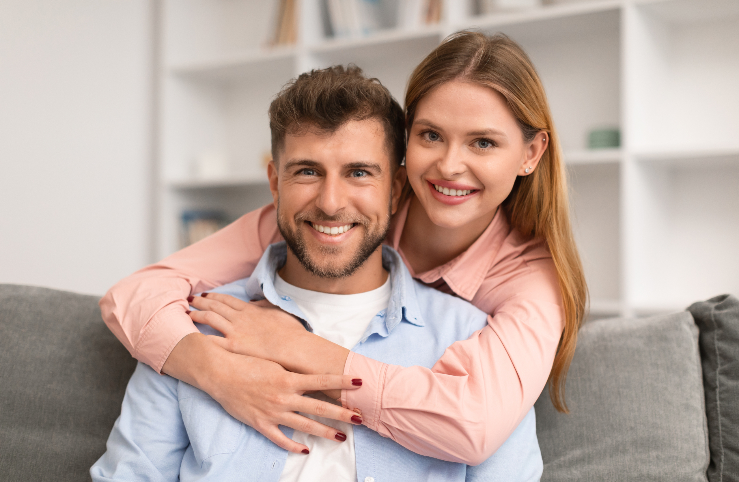 Smiling couple embracing on a couch at home, reflecting the comfortable dental experience patients find in the San Diego community 