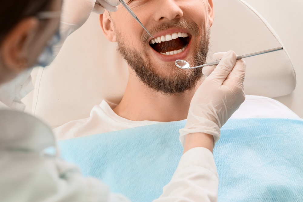 Dental Exam in Progress: Dentist Checking Patient's Teeth with Hand Instruments Dentist examining a male patient's teeth with a mirror and explorer during a dental exam in the San Diego area