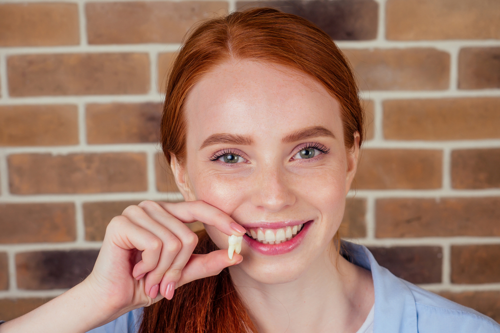Tooth Extraction Results: Redheaded Woman Holding Extracted Wisdom Tooth Smiling redheaded woman holding an extracted wisdom tooth after a tooth extraction in the San Diego community